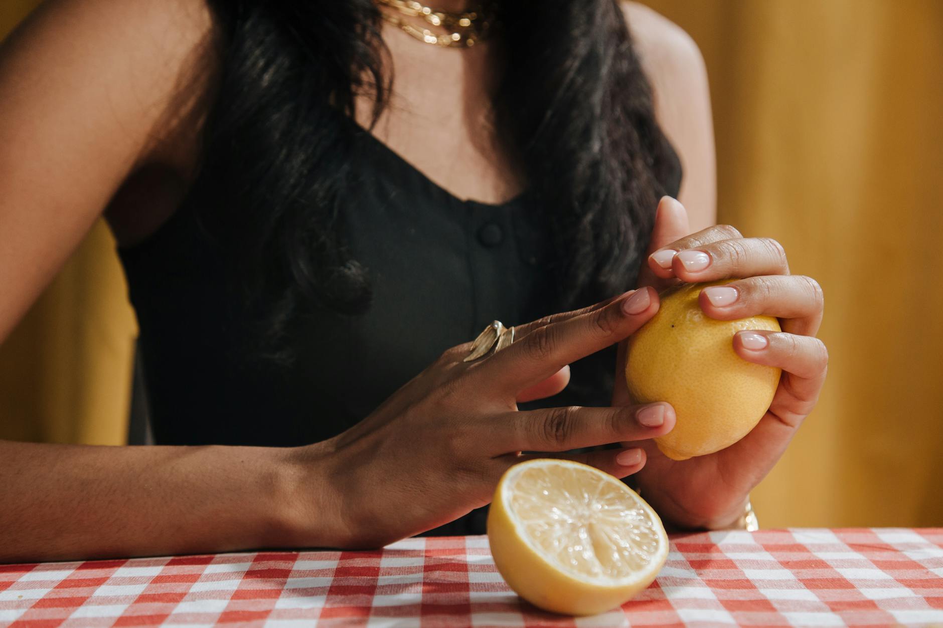 Woman holding fresh lemon at dining table, symbolic of natural sensuality and self-care