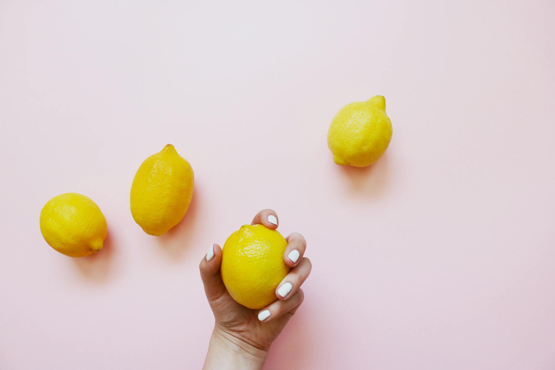 Hand holding a fresh lemon on soft pink background surrounded by lemons, representing natural pleasure and sensuality
