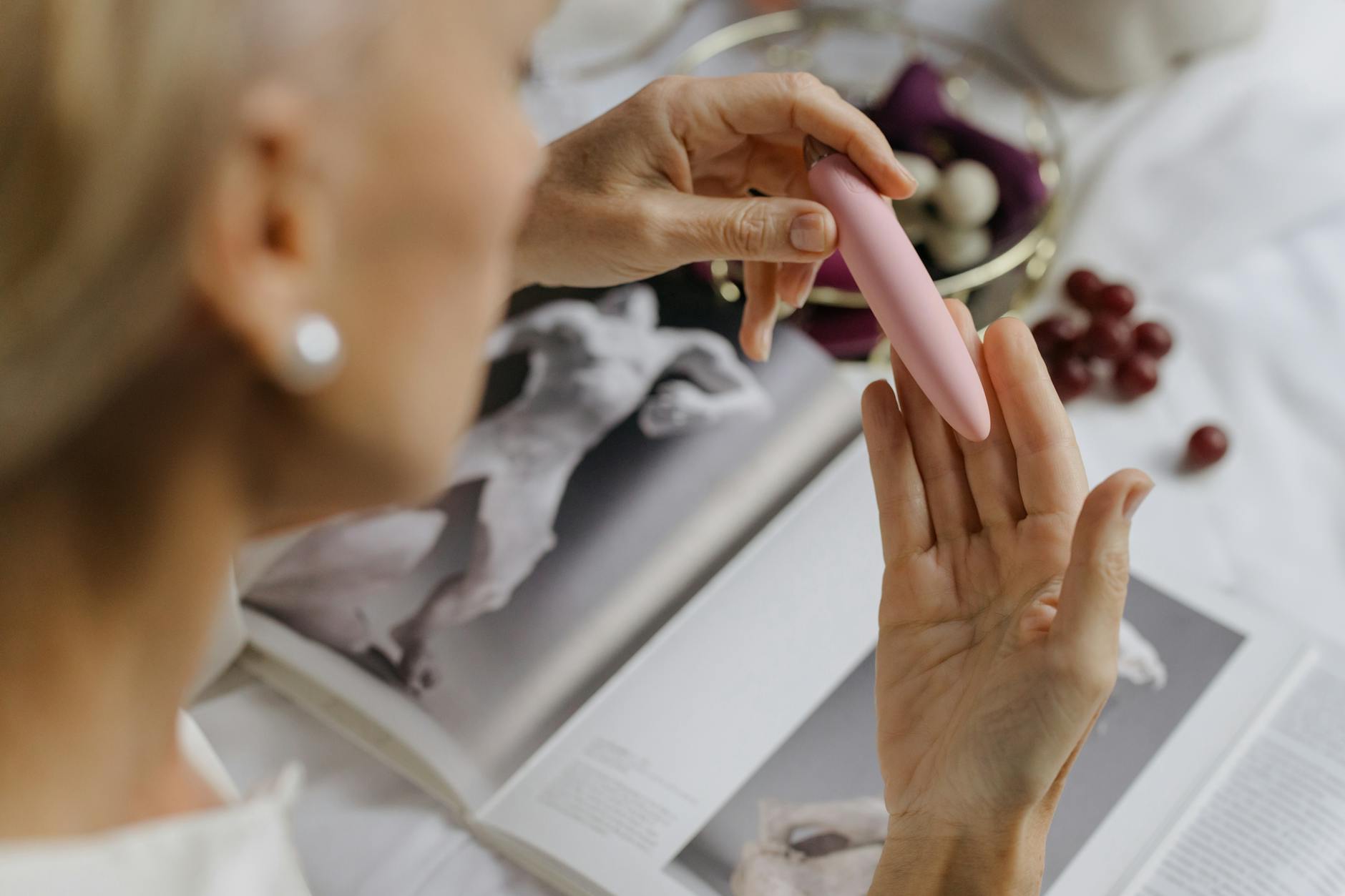 A woman holding a pink vibrator with art books in the background, emphasizing intimate reconnection and personal pleasure.