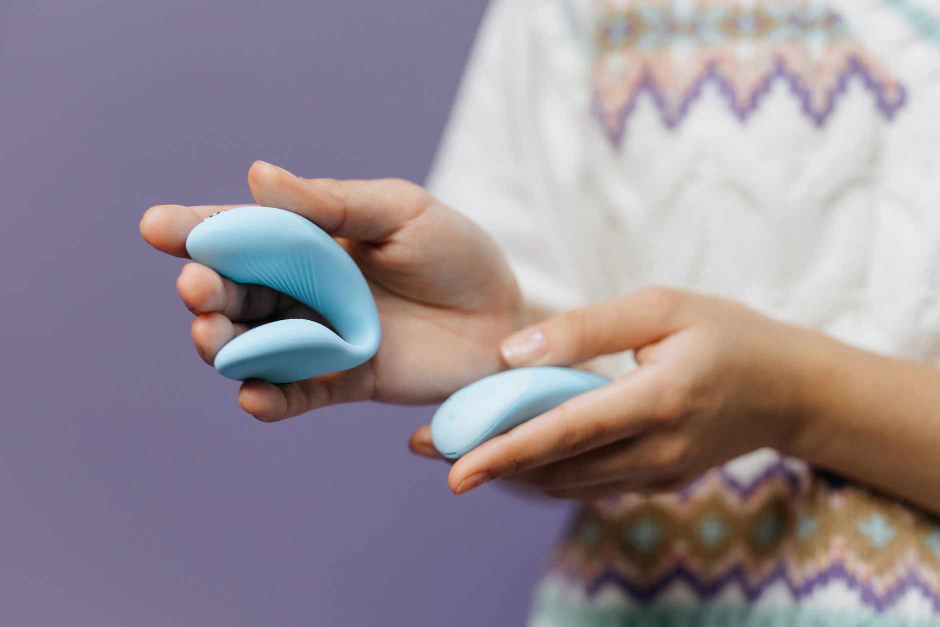 Hands holding a sleek lemon vibrator against a purple background, representing intimate pleasure and nervous system healing.