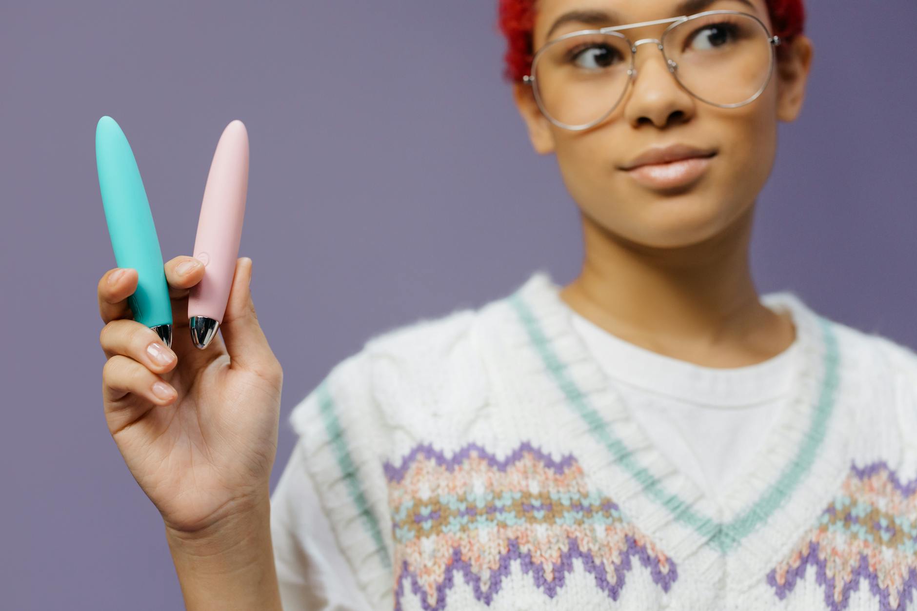 Woman holding blue and pink silicone vibrators thoughtfully, exploring clitoral stimulation options