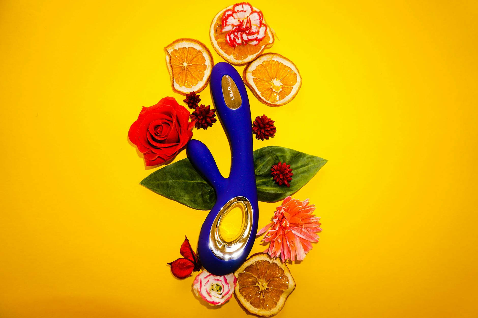A blue lemon vibrator surrounded by fresh lemons and flowers on a yellow background.